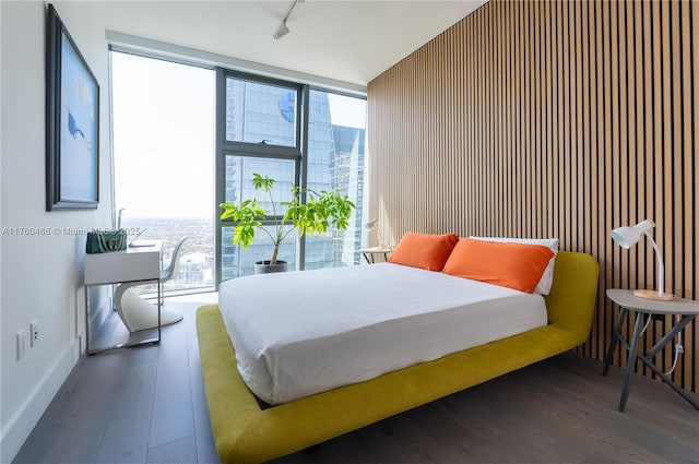 bedroom with track lighting, floor to ceiling windows, baseboards, and wood finished floors