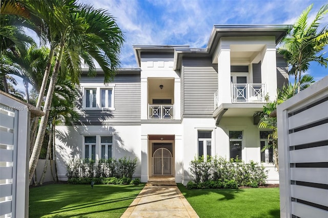 view of front of house with stucco siding, a balcony, and a front lawn