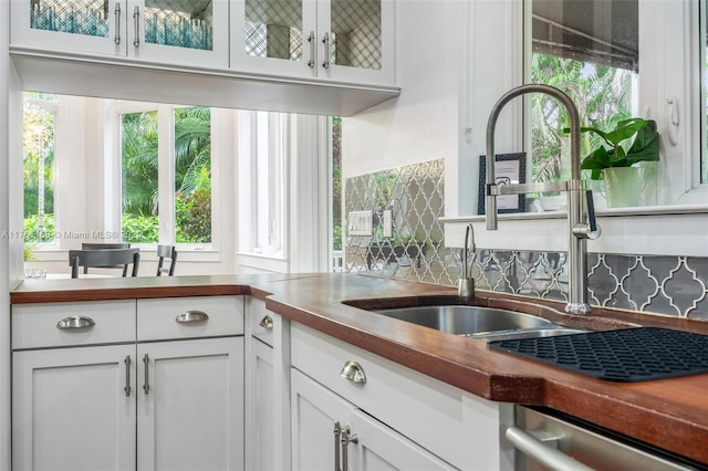 kitchen with glass insert cabinets, decorative backsplash, stainless steel dishwasher, white cabinets, and a sink