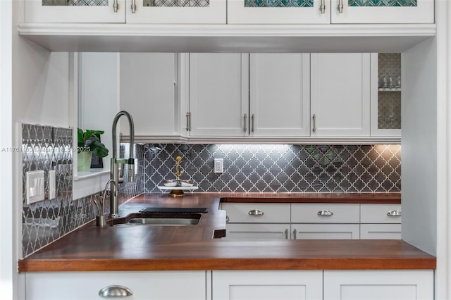 kitchen featuring tasteful backsplash, white cabinets, wooden counters, and a sink