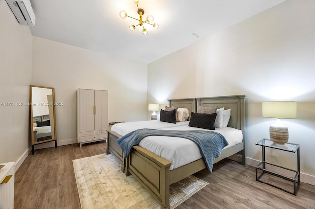 bedroom with an AC wall unit, a notable chandelier, wood finished floors, and baseboards