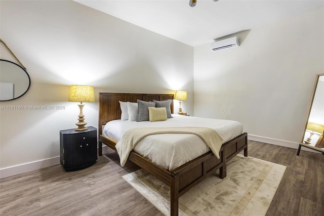 bedroom featuring baseboards, a wall unit AC, and wood finished floors