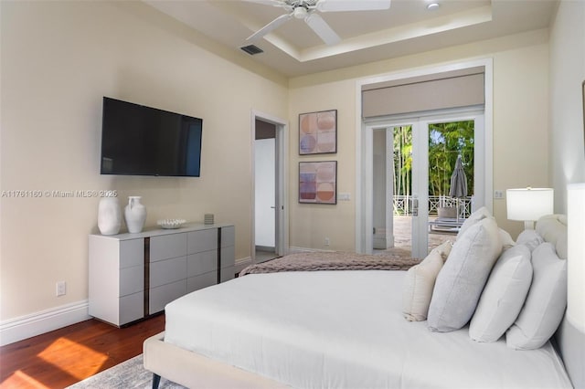 bedroom with visible vents, dark wood-type flooring, baseboards, a raised ceiling, and access to outside