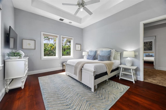 bedroom with baseboards, a raised ceiling, visible vents, and wood finished floors