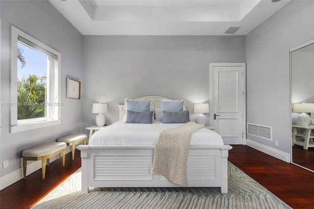 bedroom with visible vents, baseboards, a raised ceiling, and wood finished floors