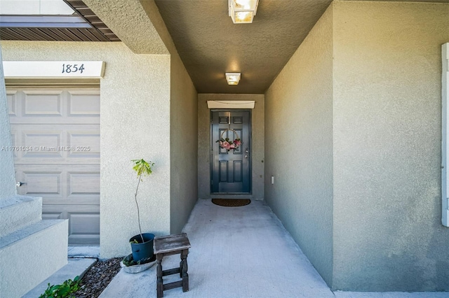 view of exterior entry with an attached garage and stucco siding