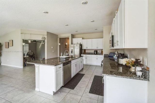 kitchen with dark stone counters, light tile patterned flooring, an island with sink, white cabinets, and appliances with stainless steel finishes