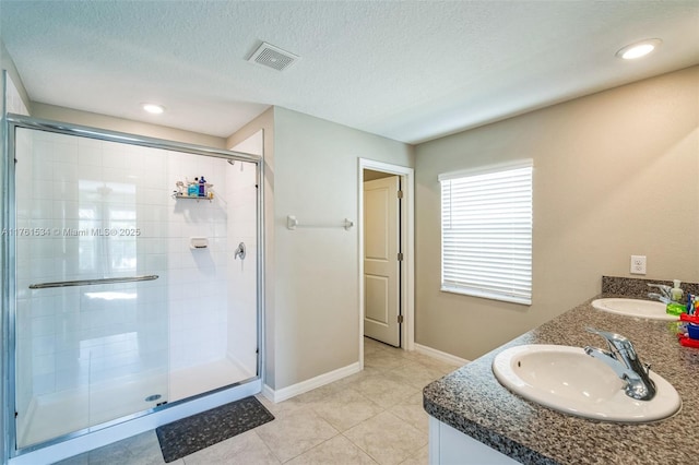 full bath with a textured ceiling, a shower stall, visible vents, and a sink