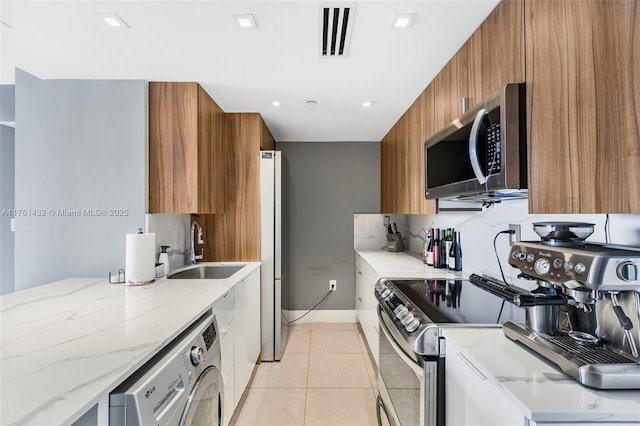 kitchen featuring brown cabinets, washer / clothes dryer, stainless steel appliances, modern cabinets, and a sink