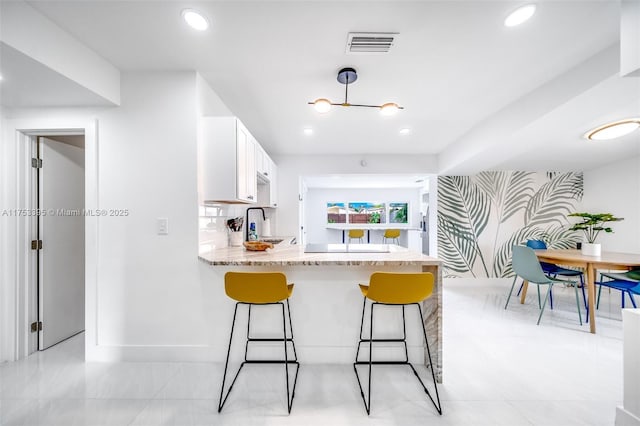 kitchen with visible vents, a kitchen breakfast bar, white cabinets, wallpapered walls, and an accent wall