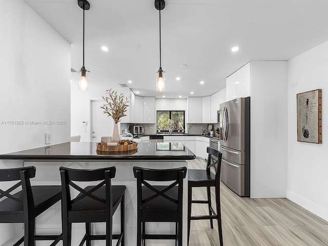 kitchen featuring a peninsula, freestanding refrigerator, white cabinets, dark countertops, and tasteful backsplash