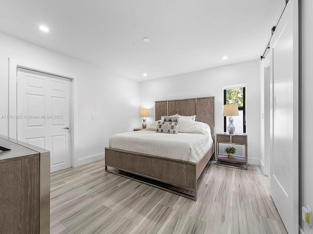 bedroom with a barn door, recessed lighting, light wood-style floors, and baseboards