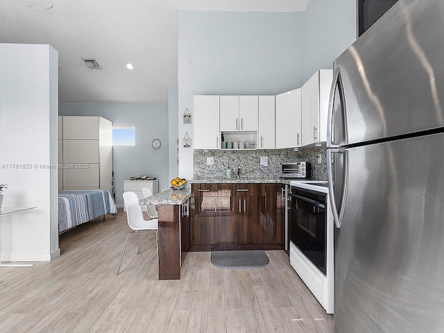 kitchen with visible vents, light wood finished floors, freestanding refrigerator, white cabinetry, and range