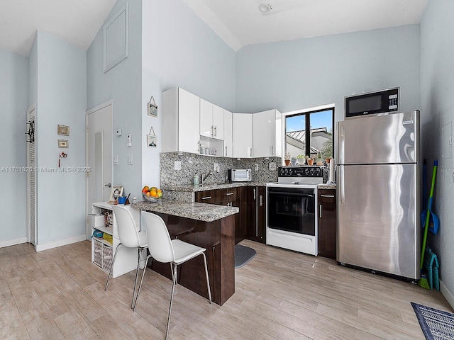 kitchen featuring a peninsula, light wood-style flooring, freestanding refrigerator, electric range oven, and black microwave