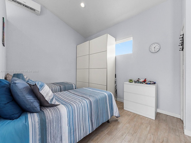 bedroom featuring lofted ceiling, light wood-style floors, baseboards, and a wall mounted AC