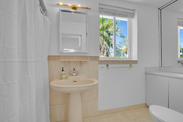 bathroom featuring toilet, a shower with shower curtain, tile patterned flooring, and tile walls