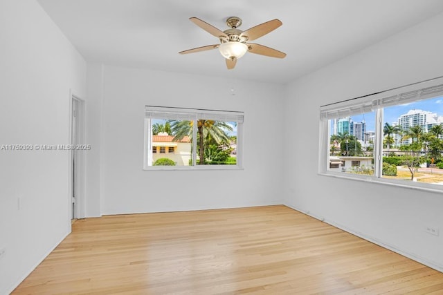 spare room with a wealth of natural light, a view of city, light wood-style floors, and ceiling fan