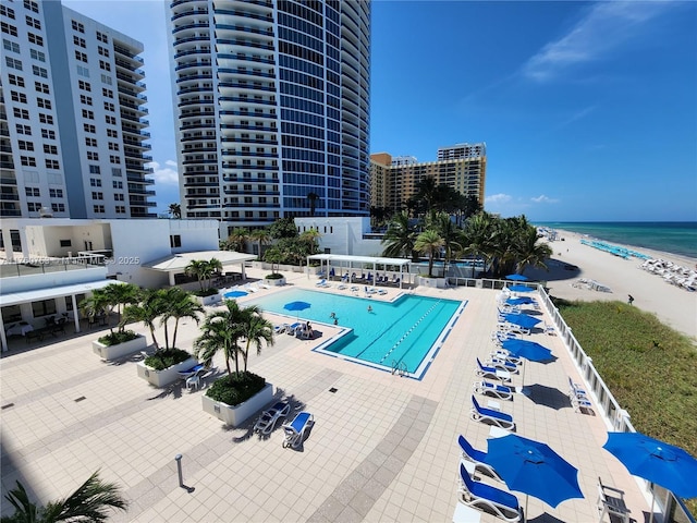 community pool with a water view, a beach view, and a patio