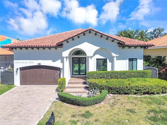 mediterranean / spanish house featuring a gate, stucco siding, french doors, a garage, and decorative driveway