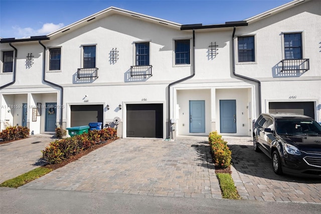 townhome / multi-family property with decorative driveway, a garage, and stucco siding