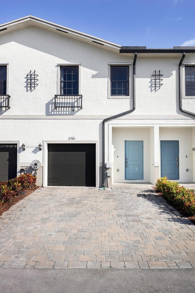 view of front of home with a balcony, stucco siding, decorative driveway, and a garage