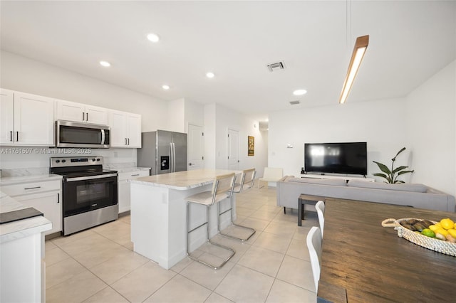 kitchen with a kitchen island, stainless steel appliances, white cabinetry, open floor plan, and a kitchen bar