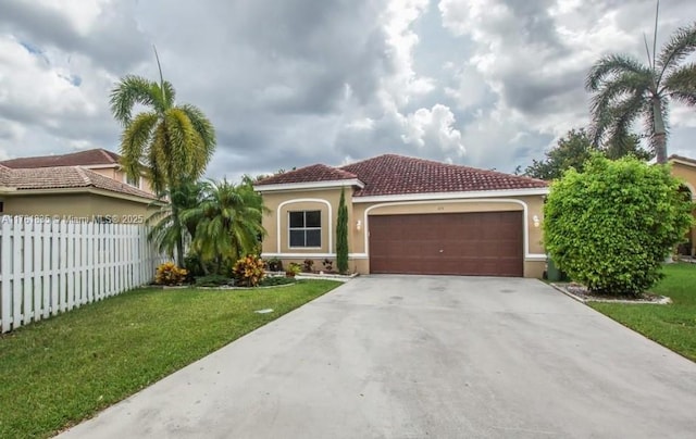 mediterranean / spanish-style house with a front yard, fence, an attached garage, stucco siding, and concrete driveway