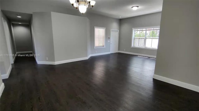 unfurnished room with a chandelier, dark wood-type flooring, and baseboards