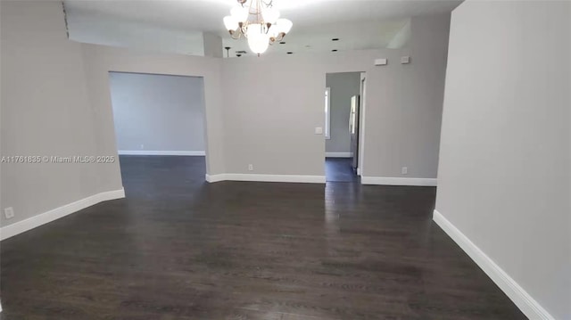 spare room with baseboards, a chandelier, and dark wood-style flooring