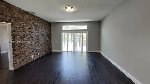 empty room with baseboards, visible vents, dark wood-style flooring, and a textured ceiling