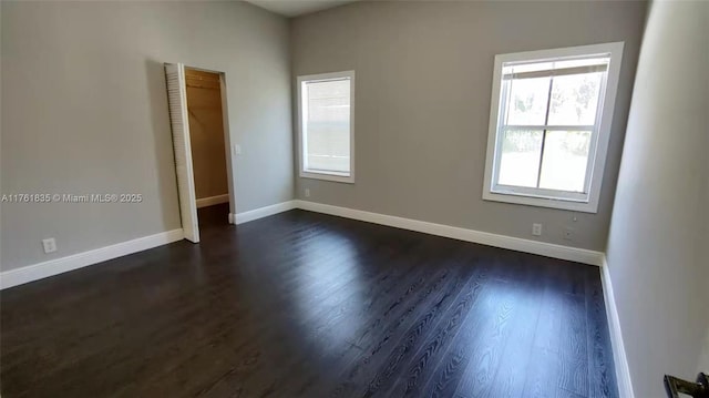 spare room featuring a wealth of natural light, baseboards, and dark wood-style floors