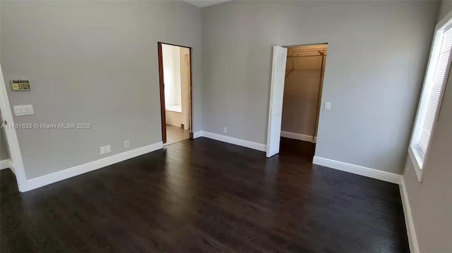 unfurnished bedroom featuring ensuite bath, baseboards, and dark wood-style flooring