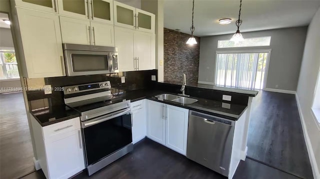 kitchen with a sink, dark countertops, appliances with stainless steel finishes, a peninsula, and white cabinets