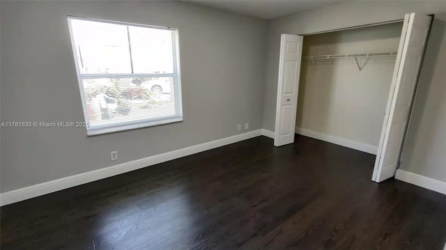 unfurnished bedroom with a closet, baseboards, and dark wood-style flooring