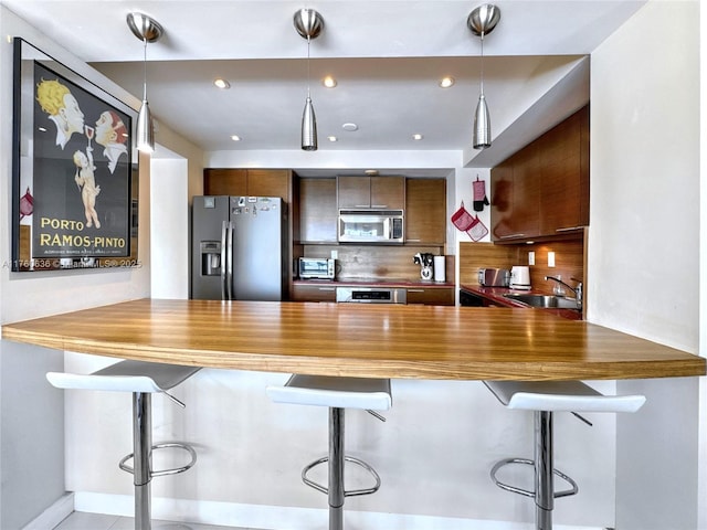 kitchen with a sink, appliances with stainless steel finishes, a peninsula, decorative backsplash, and hanging light fixtures