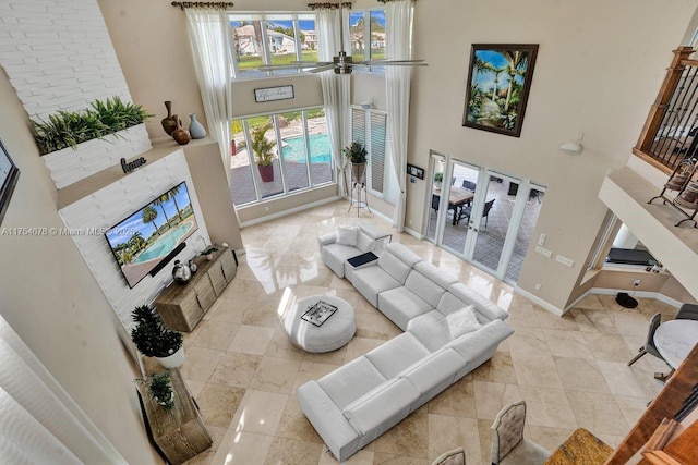 living area with ceiling fan, a high ceiling, and baseboards