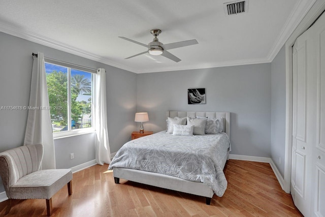 bedroom with wood finished floors, visible vents, baseboards, a closet, and crown molding