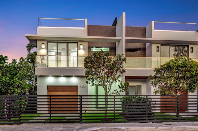 modern home featuring a fenced front yard, a balcony, an attached garage, and stucco siding