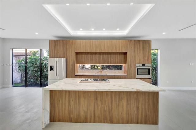 kitchen with modern cabinets, a sink, a tray ceiling, a spacious island, and appliances with stainless steel finishes