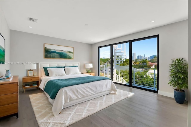 bedroom with visible vents, baseboards, a city view, wood finished floors, and access to outside