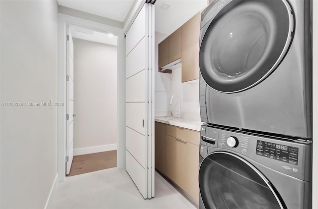 clothes washing area with stacked washer / dryer, cabinet space, baseboards, and a sink