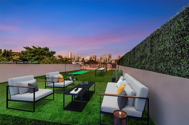 yard at dusk featuring an outdoor hangout area, a view of city, and fence