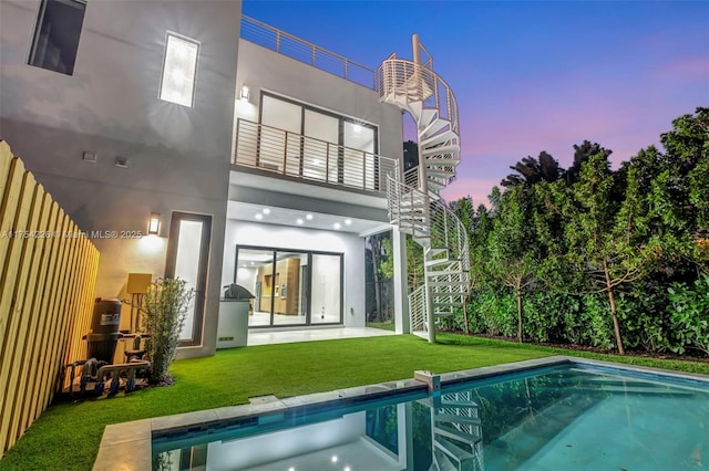 back of house with stairs, a balcony, a yard, and an outdoor pool