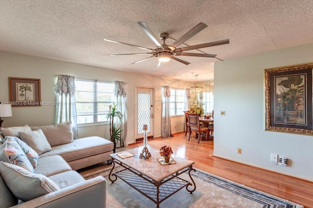 living room featuring ceiling fan, baseboards, a textured ceiling, and light wood-style flooring