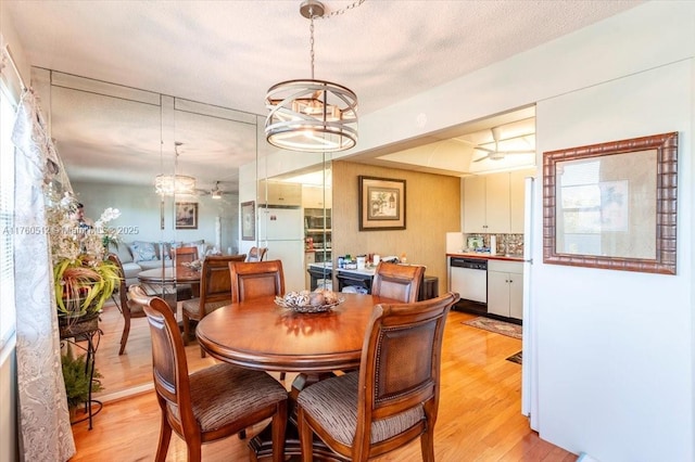 dining area with a raised ceiling, a textured ceiling, an inviting chandelier, and light wood finished floors