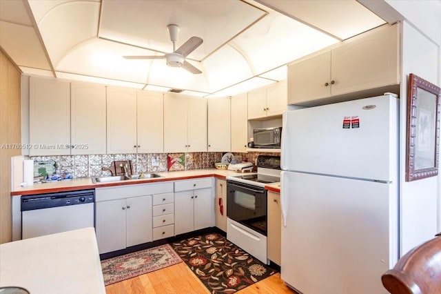 kitchen with a sink, backsplash, light countertops, white appliances, and dark wood-style flooring