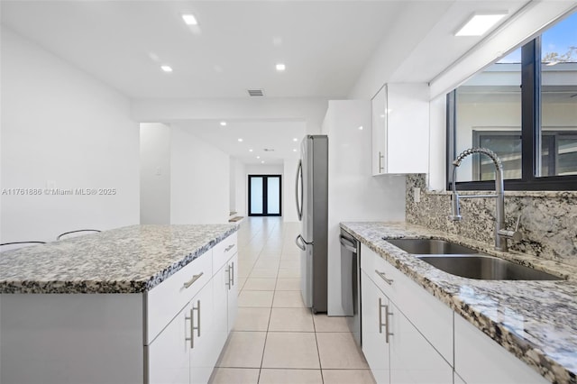 kitchen featuring backsplash, light stone counters, appliances with stainless steel finishes, white cabinets, and a sink