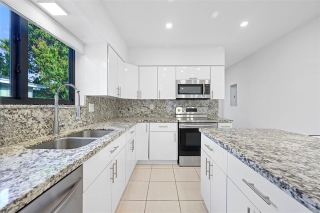 kitchen with light tile patterned floors, white cabinetry, a sink, stainless steel appliances, and decorative backsplash