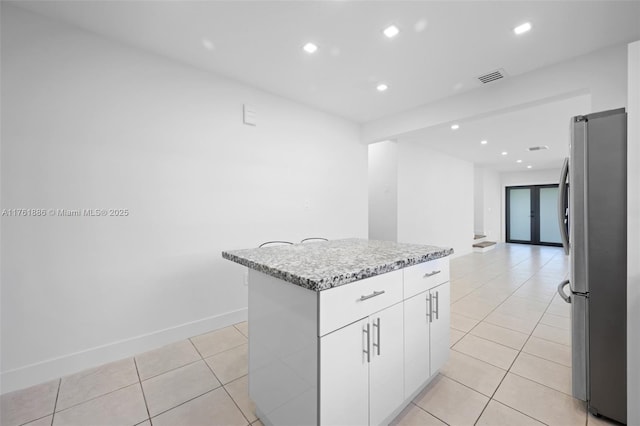 kitchen with visible vents, a center island, light tile patterned floors, freestanding refrigerator, and white cabinets