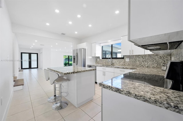 kitchen with light stone counters, a sink, white cabinets, appliances with stainless steel finishes, and backsplash